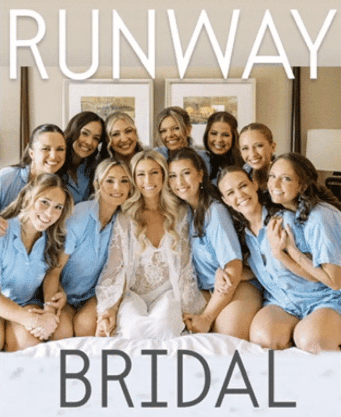 Bridal party in matching blue shirts posing around bride in lace robe on bed.