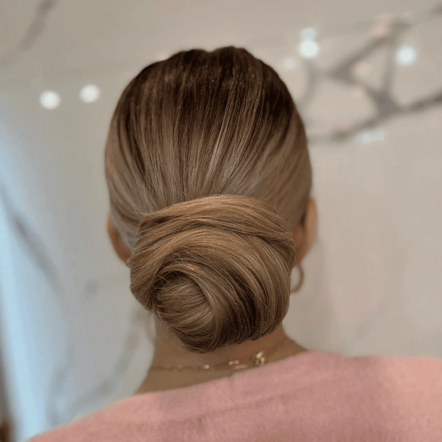 Back view of a person with a sleek, twisted bun hairstyle and wearing a pink top.