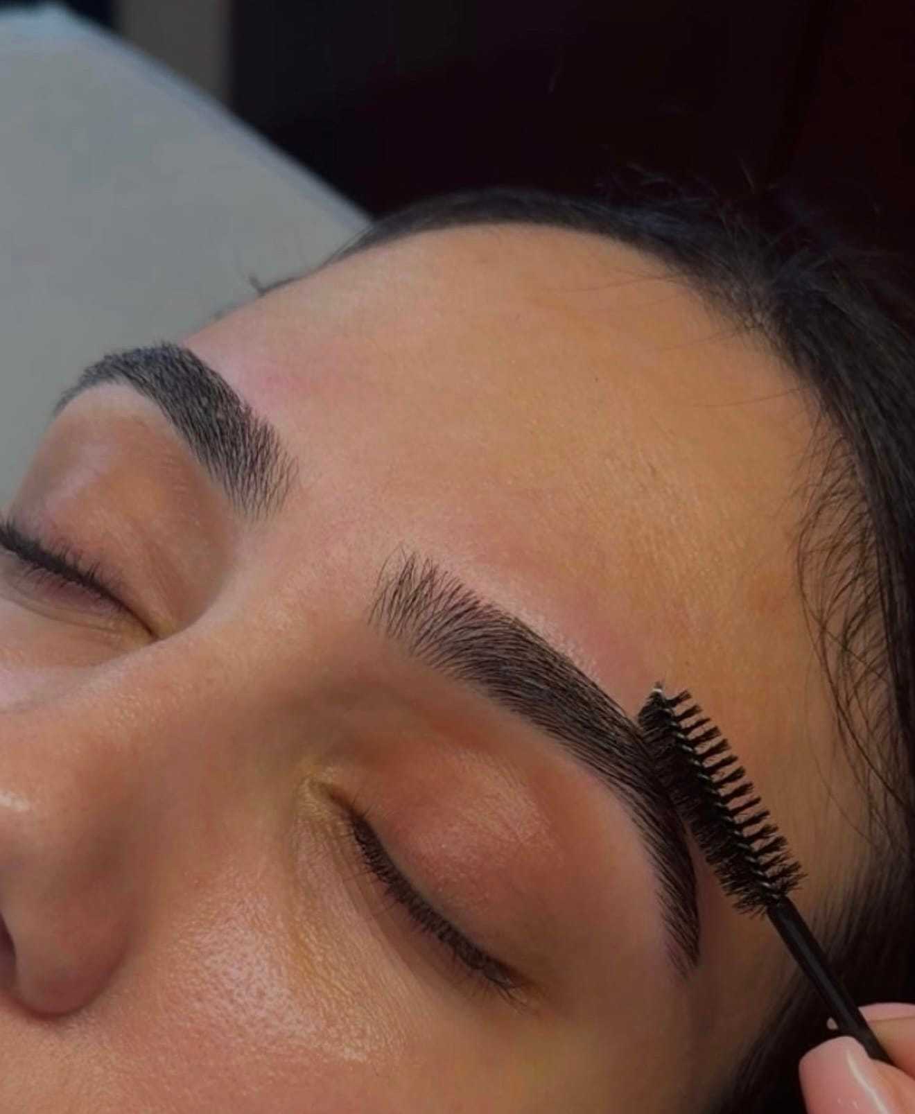 Eyebrow being groomed with a brush on closed-eyed person.