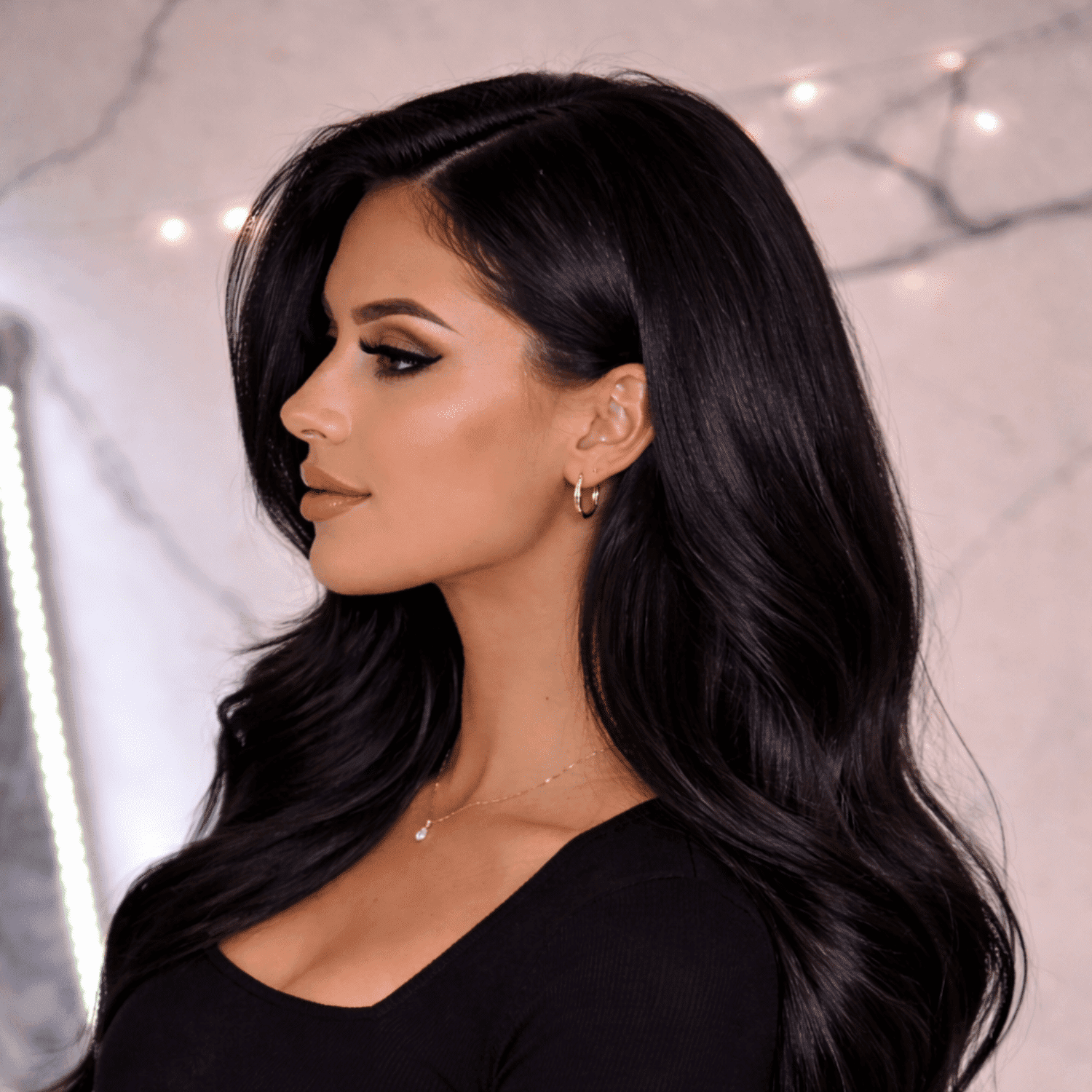 Elegant woman with long dark hair, hoop earrings, and a black top, in a softly lit room.